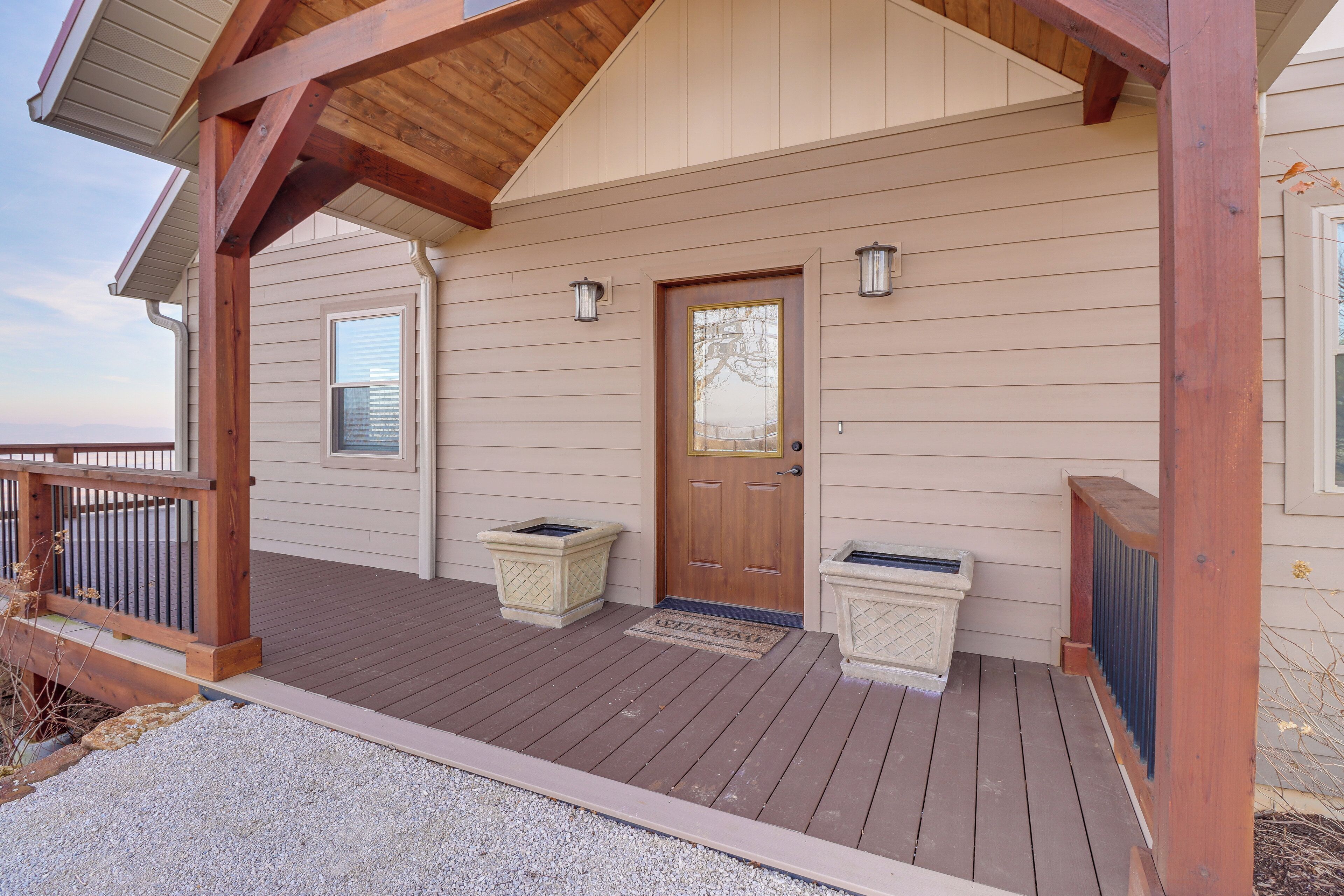 A wooden deck with a covered porch, a door with a window, and two planters.