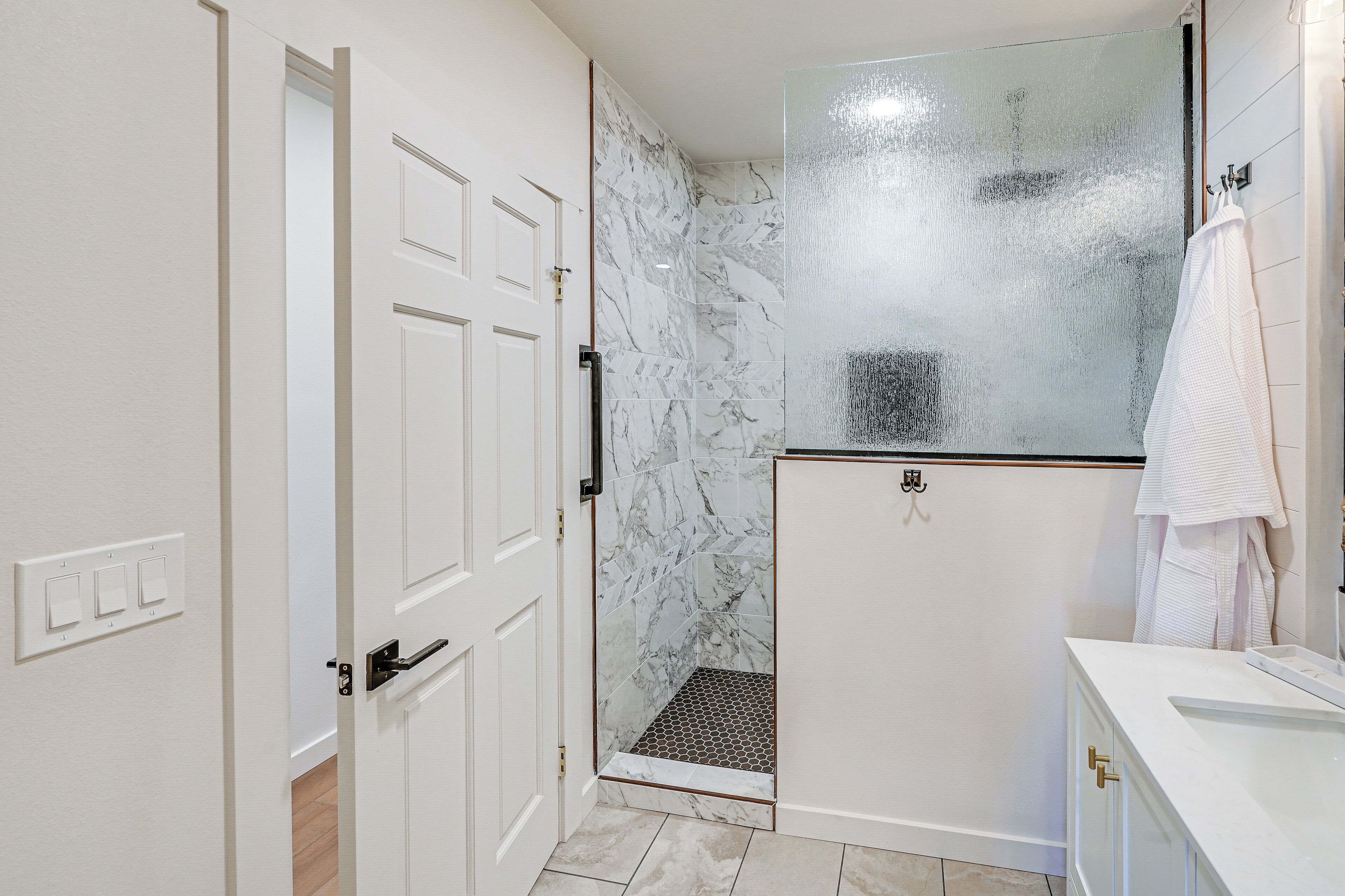 Un baño con ducha, una puerta blanca y un lavamanos blanco con una toalla colgada en la pared.
