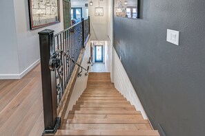 Una escalera de madera con barandilla de metal que conduce a un rellano del segundo piso con vista al interior.