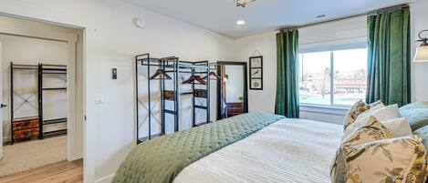 Un dormitorio con cama, armario, espejo y ventana con cortinas.