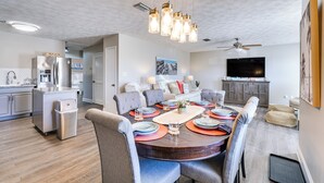 A modern kitchen with stainless steel appliances, a dining area with a round table and chairs, and a living room with a flat-screen TV and ceiling fan. - Panama City Beach House w/ Patio, Walk to Ocean (Panama City Beach)