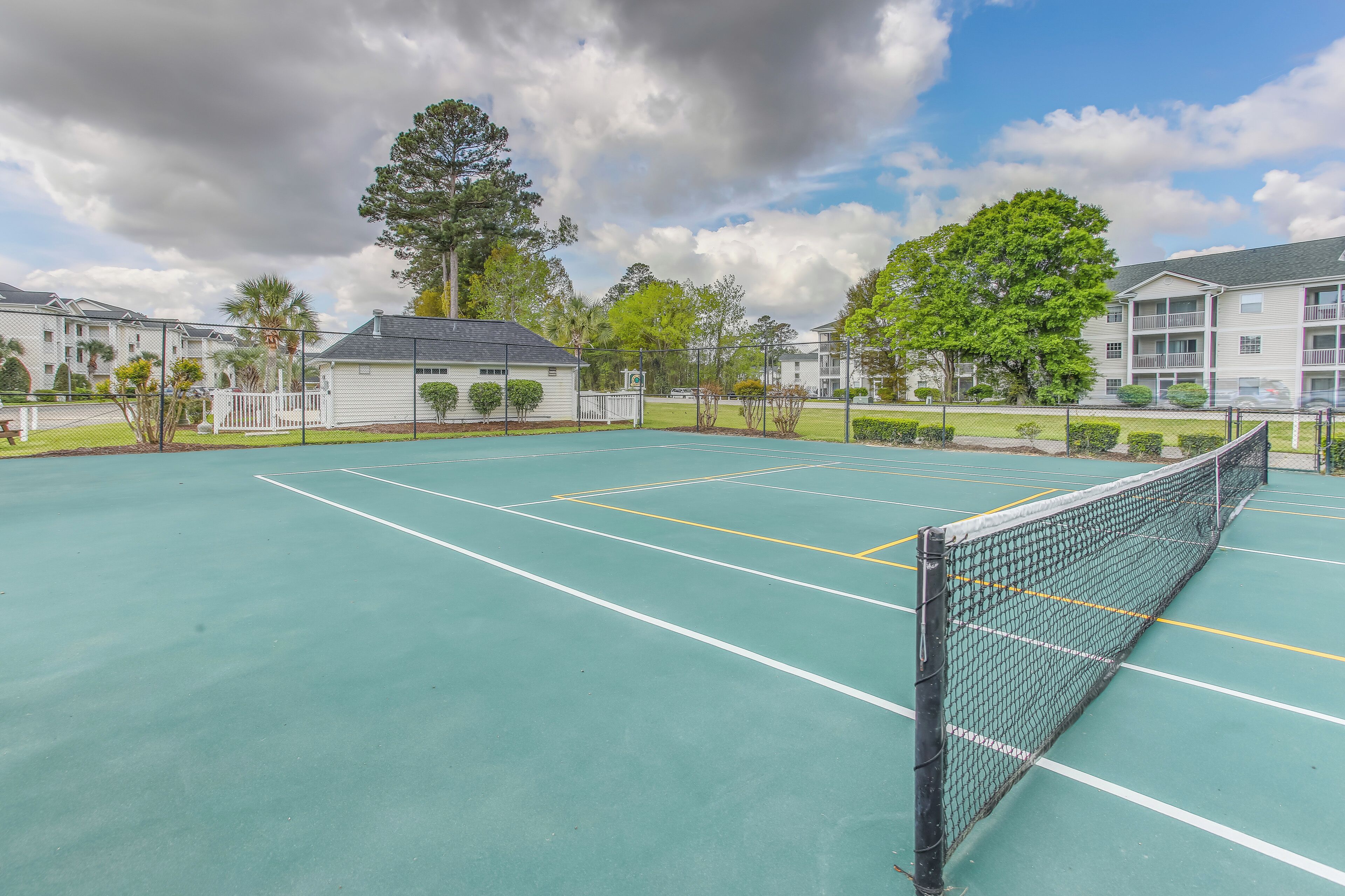 Un court de tennis avec un filet, entouré de bâtiments et d’arbres.