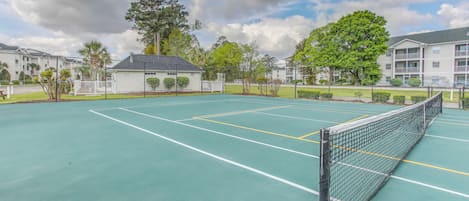 A tennis court with a net, surrounded by buildings and trees.