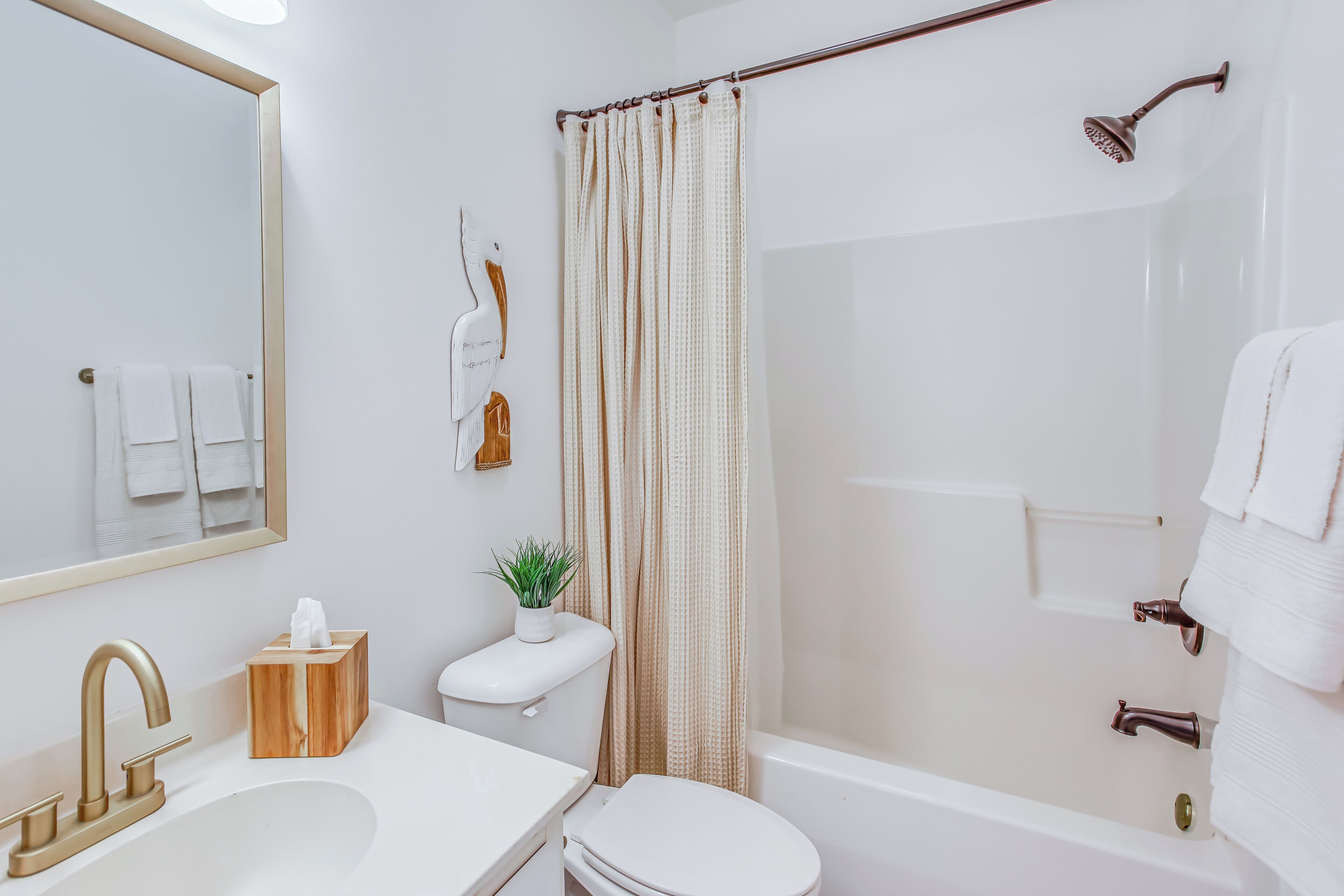 Un baño con lavamanos blanco, grifo dorado, inodoro, ducha con cortina y espejo.