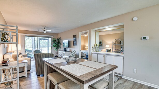 A spacious living area with a dining table, comfortable seating, a kitchen area, and a view of the outdoors. - Pawleys Island Condo w/ Screened Porch + Golfing! (Pawleys Island)
