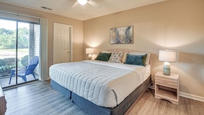 A bedroom with a large bed, two bedside lamps, a ceiling fan, and a view through a sliding glass door to the outside. - Pawleys Island Condo w/ Screened Porch + Golfing! (Pawleys Island)