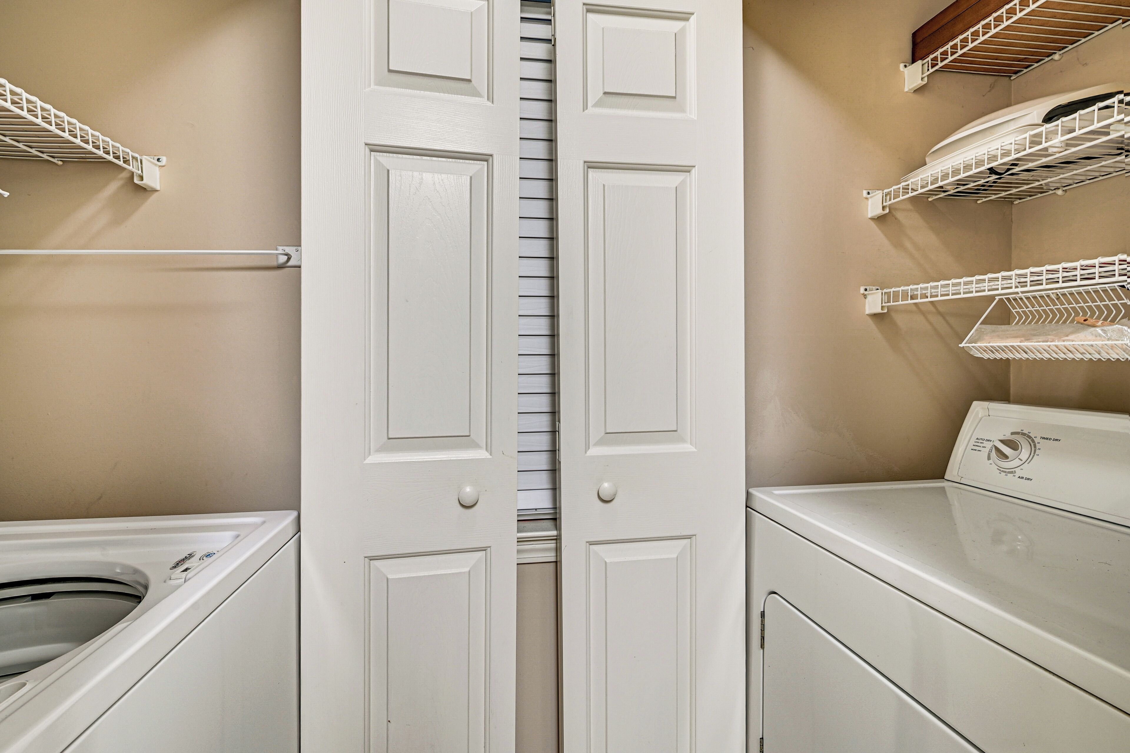 A laundry room with a white door, a washing machine, and a dryer. There are metal shelves above the dryer.