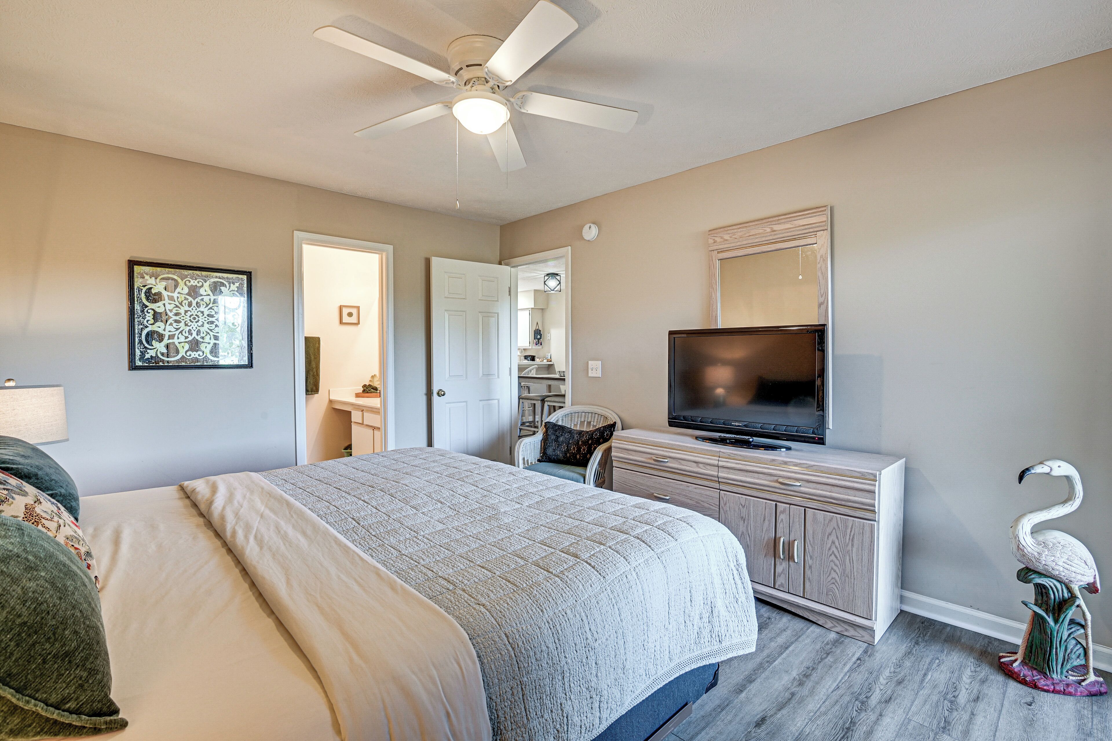 A bedroom with a bed, a television, a dresser, a ceiling fan, and a door leading to a bathroom.
