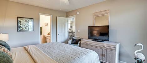 A bedroom with a bed, a television, a dresser, a ceiling fan, and a door leading to a bathroom.