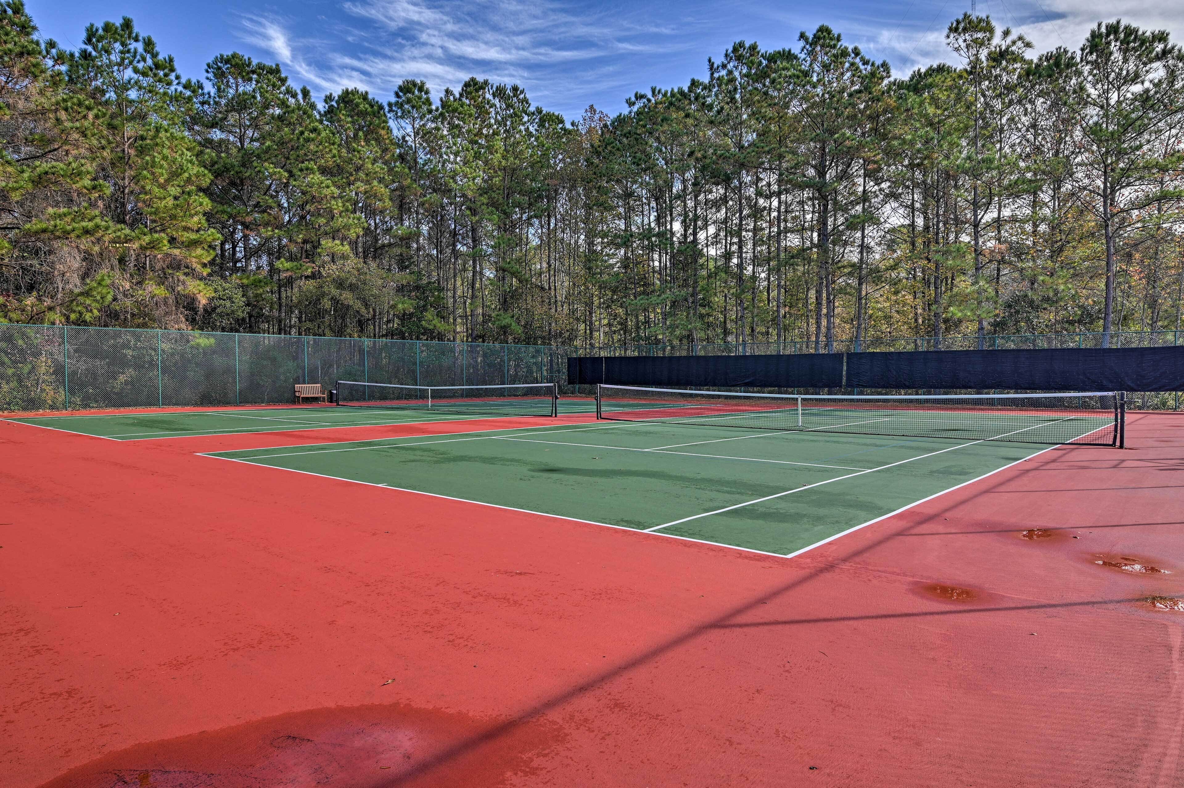 Un court de tennis avec un filet, entouré d’une clôture, et des arbres en arrière-plan.