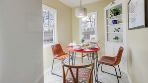 Un comedor con una mesa redonda, dos sillas, una lámpara colgante y una pizarra con escritura en la pared.