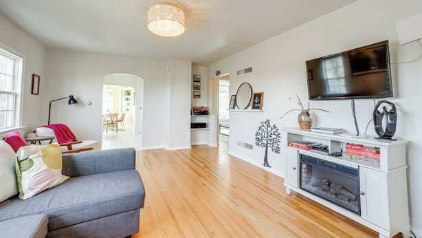 Una sala de estar moderna con un sofá gris, piso de madera, un mueble blanco para entretenimiento con un televisor y una chimenea.