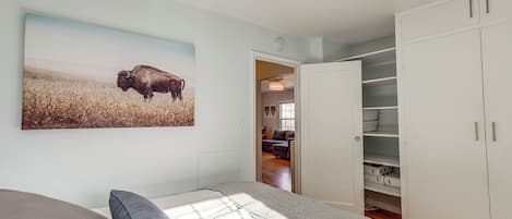 Un dormitorio con cama, almohadas, un cuadro de un búfalo y un armario.