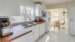 Una cocina con armarios blancos, encimera de madera, un lavamanos y una zona de comedor con mesa y sillas.