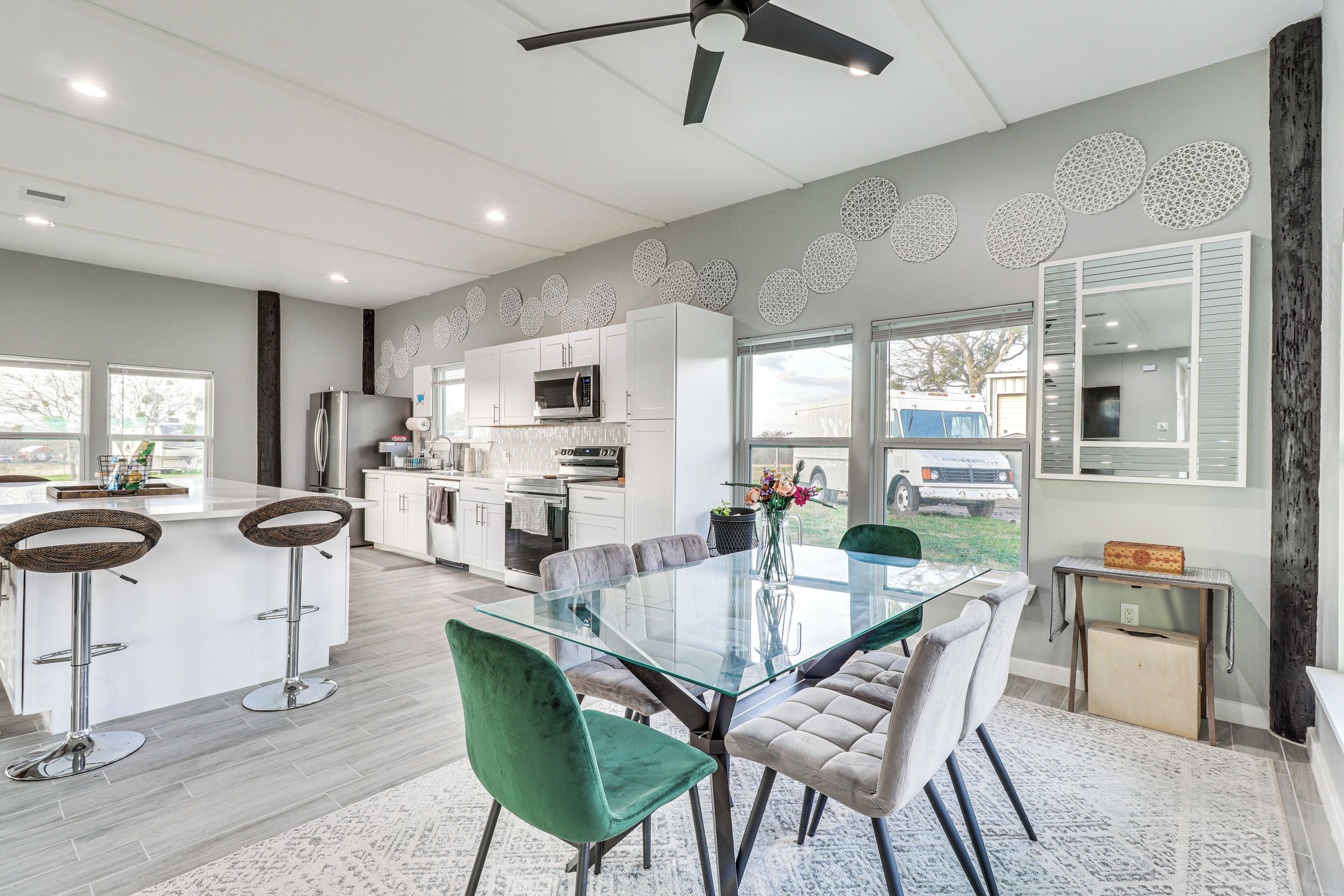A modern kitchen with white cabinets, a microwave, and a refrigerator. There is a dining area with a glass table and chairs.