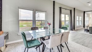 A spacious dining area with a glass table and modern chairs, large windows offering a view of the outdoors, and a ceiling fan. - Modern Farmhouse in Del Valle: Rural Setting! (Del Valle)