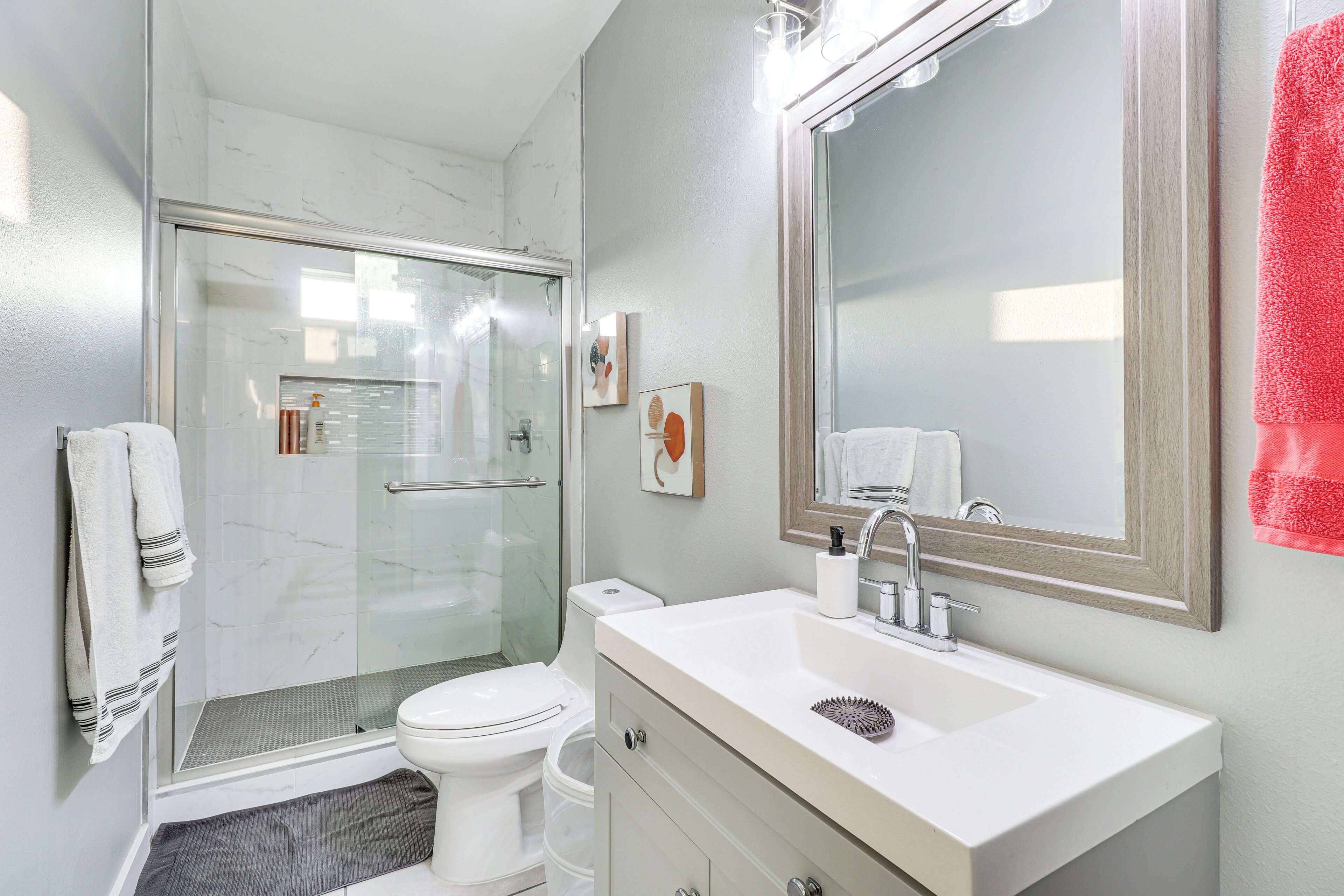 A modern bathroom with a glass shower enclosure, a white toilet, a sink with a mirror, and a red towel on the wall.