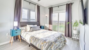 A modern bedroom with a bed, bedside tables, a ceiling fan, and a large window with curtains. - Modern Farmhouse in Del Valle: Rural Setting! (Del Valle)
