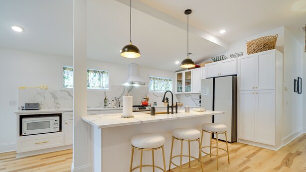 Une cuisine moderne avec des meubles blancs, un îlot central doté de tabourets, un éclairage suspendu et un four à micro-ondes.