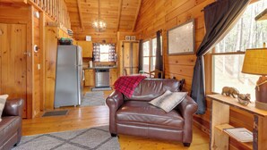 Un interior acogedor de cabaña con un sofá de cuero marrón, una mesa de comedor con una lámpara y una zona de cocina.
