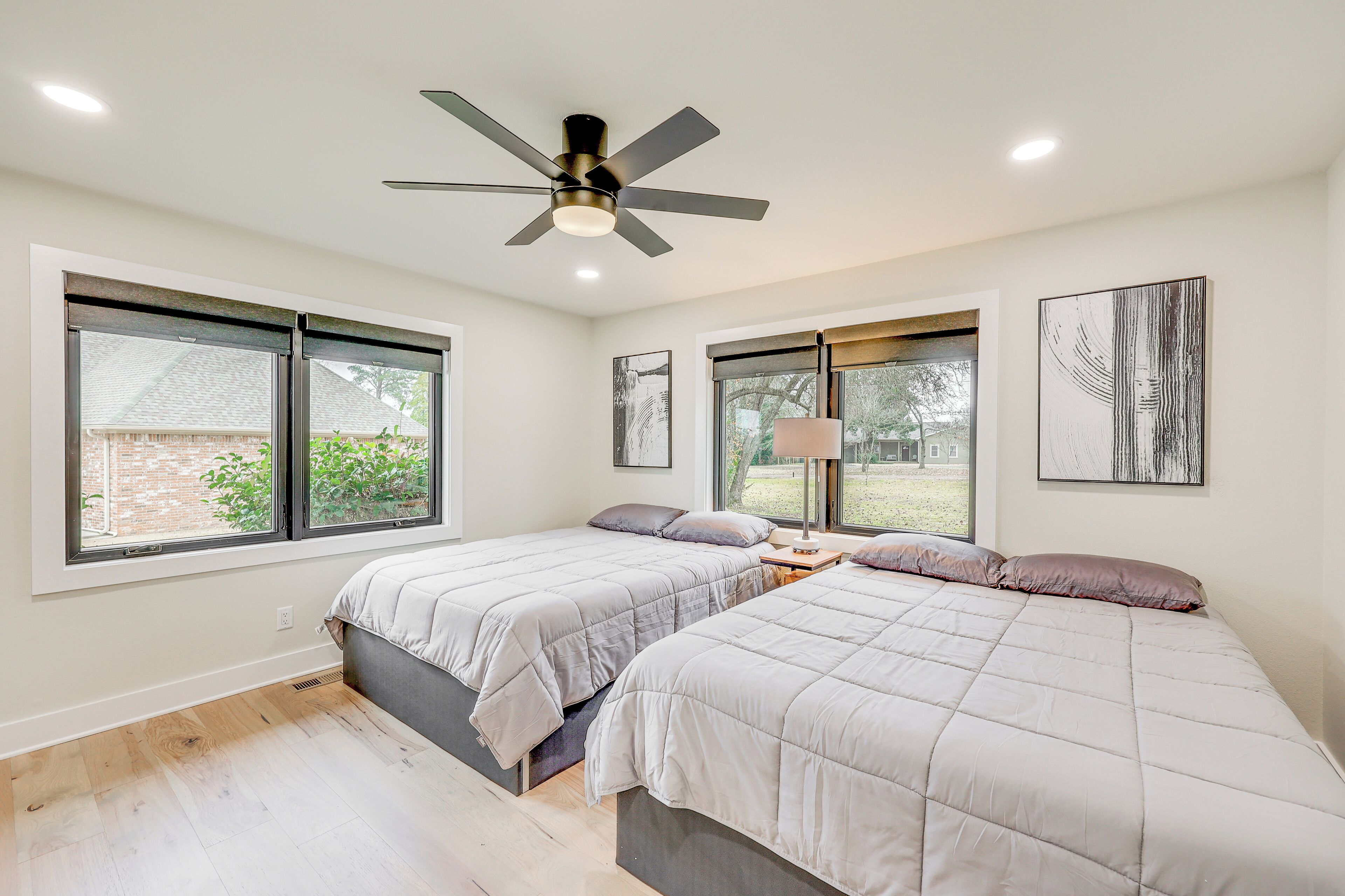 A bedroom with two beds, a ceiling fan, and large windows.