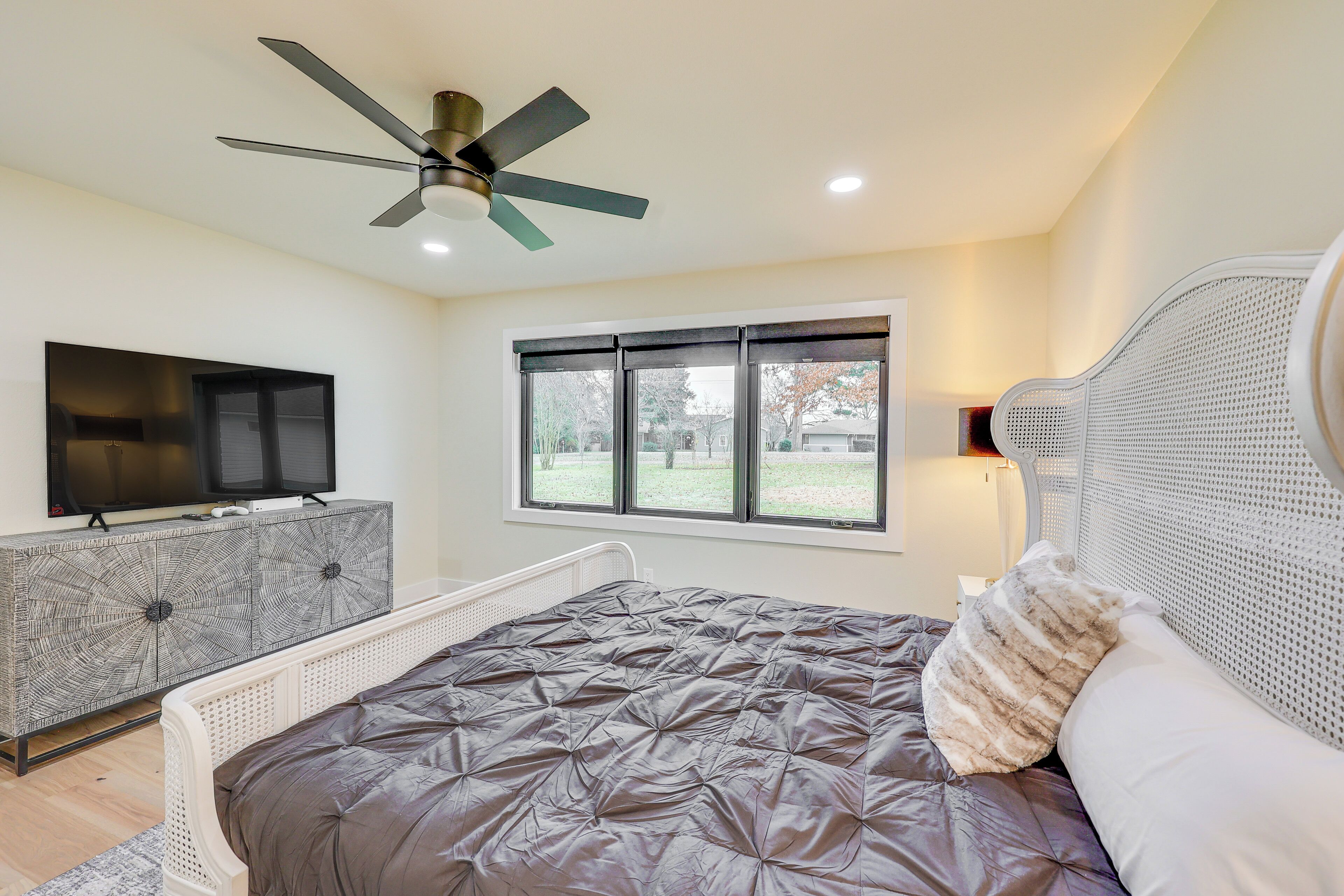 A bedroom with a bed, a ceiling fan, a TV, a window, and a nightstand.