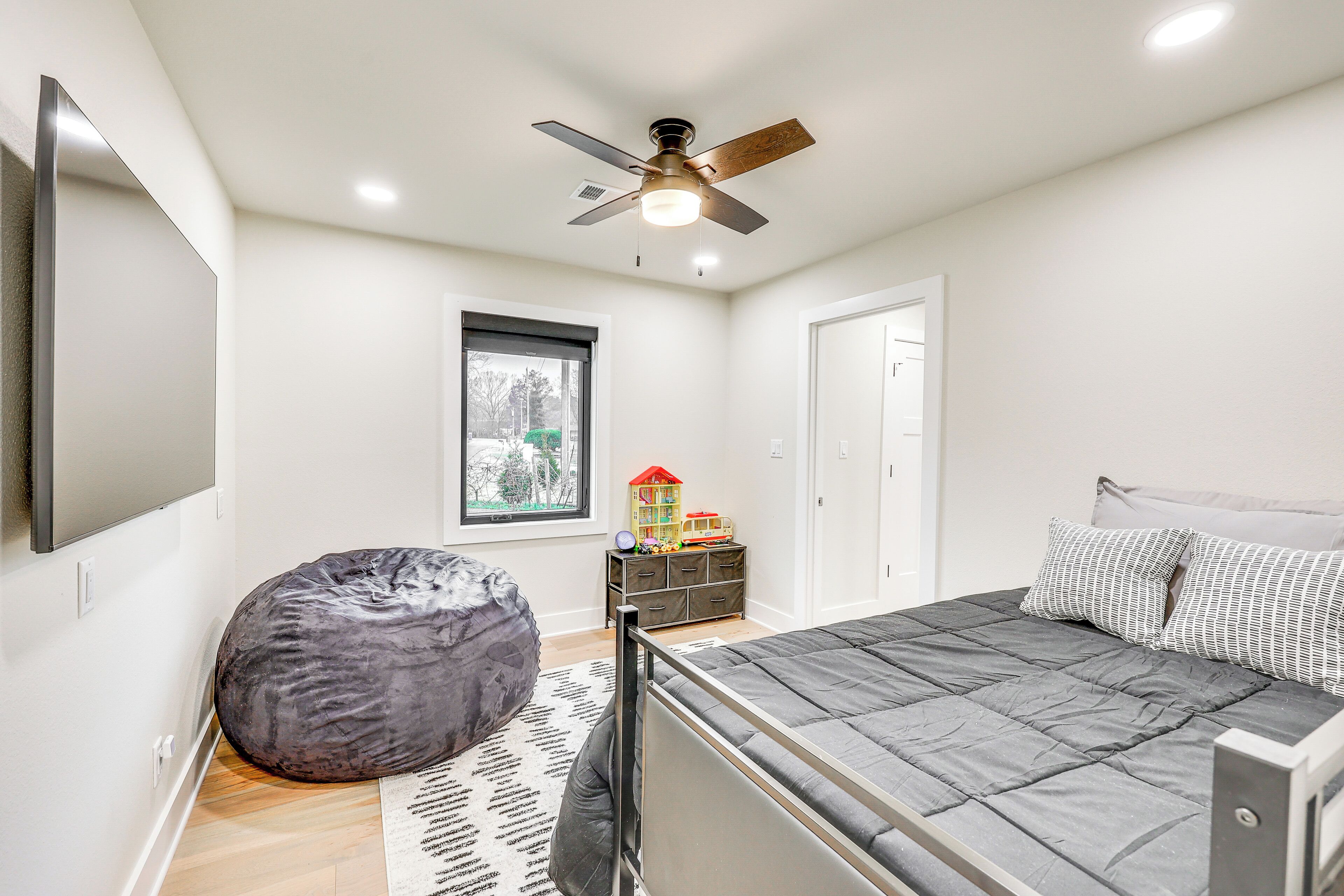 A bedroom with a bed, a ceiling fan, a window, a dresser, and a bean bag chair.