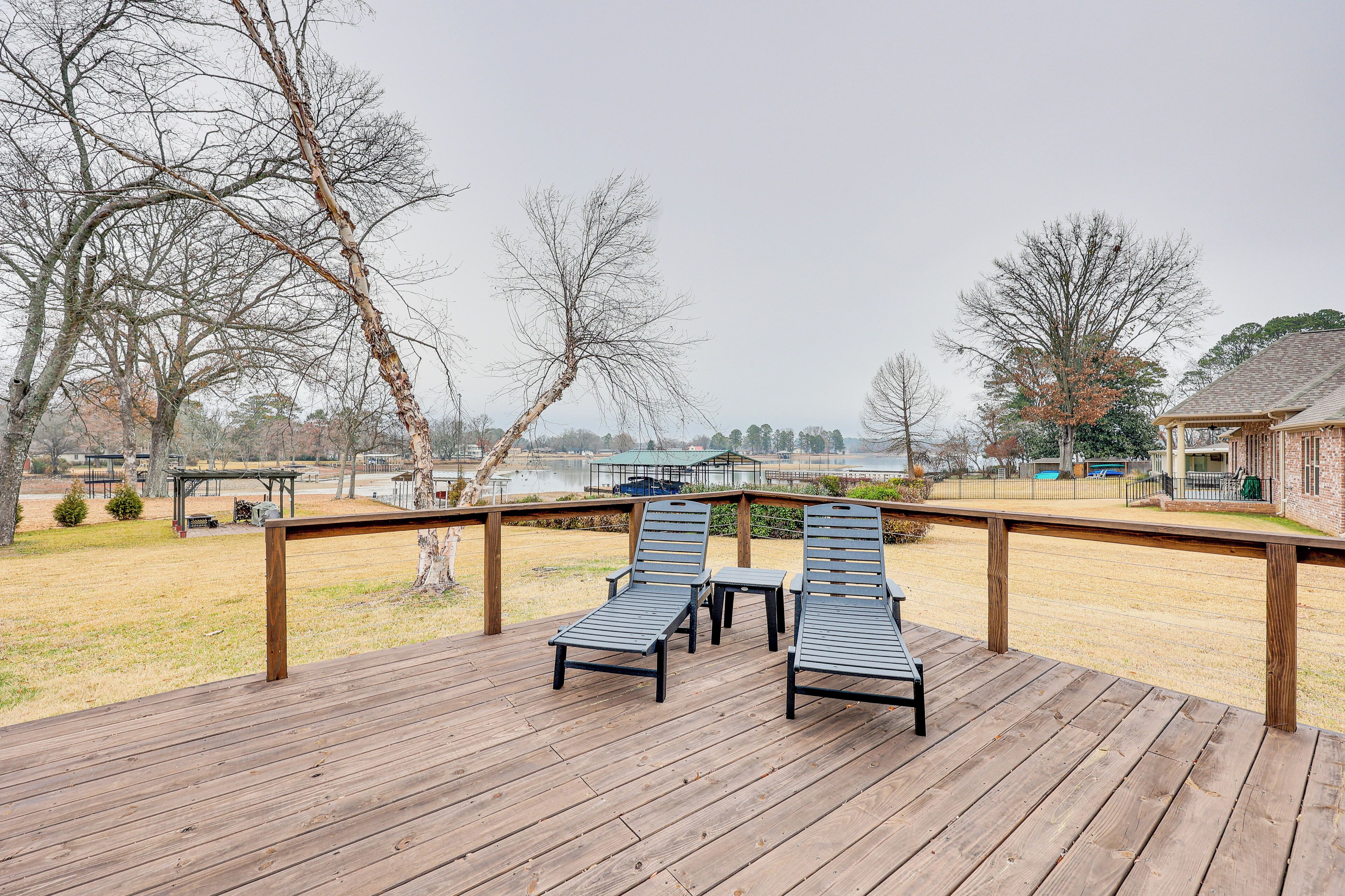 A wooden deck with two lounge chairs and a small table, overlooking a grassy area with trees and a building in the background.