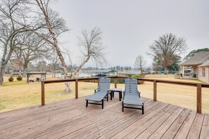 A wooden deck with two lounge chairs and a small table, overlooking a grassy area with trees and a building in the background. - Grand Lakefront Home in Hot Springs w/ Boat Dock! (Hot Springs)