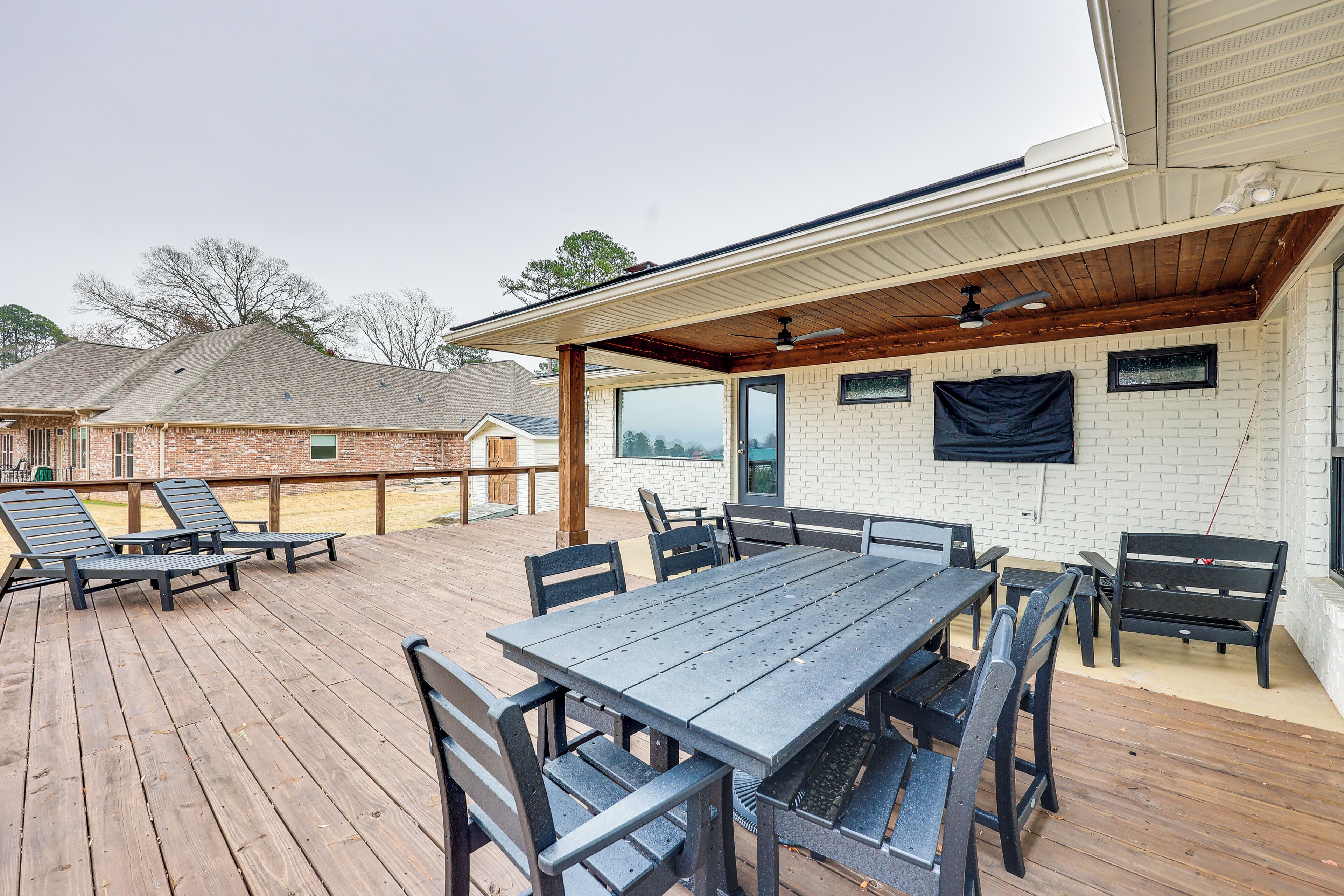 Un patio exterior con terraza de madera, una zona de estar cubierta y un muro de ladrillo.