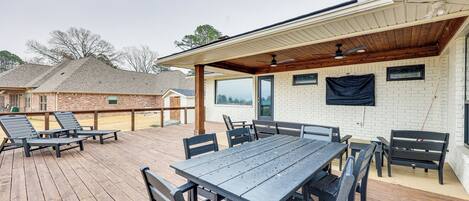 Un patio exterior con terraza de madera, una zona de estar cubierta y un muro de ladrillo.