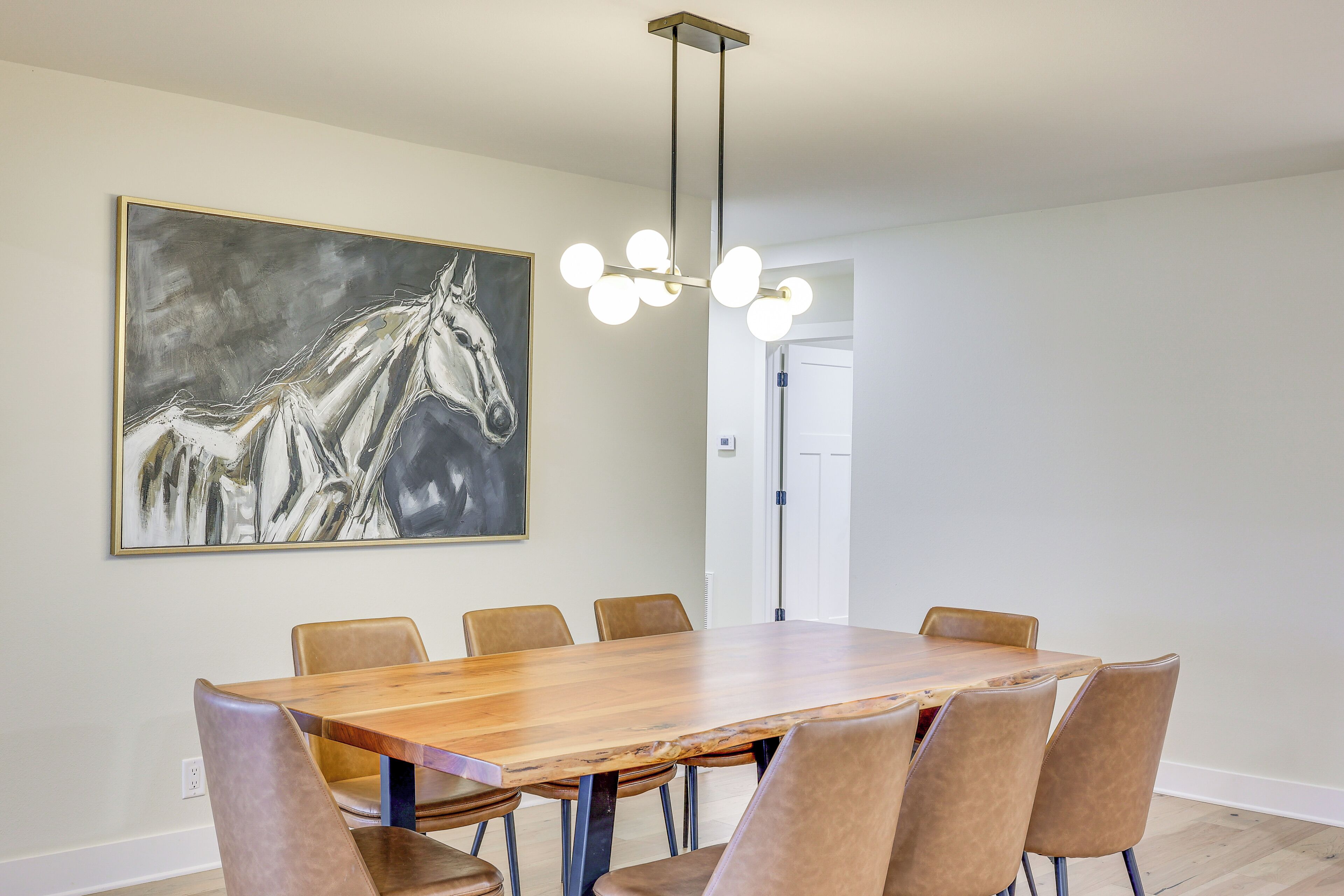 A dining area with a wooden table and six chairs, a chandelier, and a large abstract painting on the wall.
