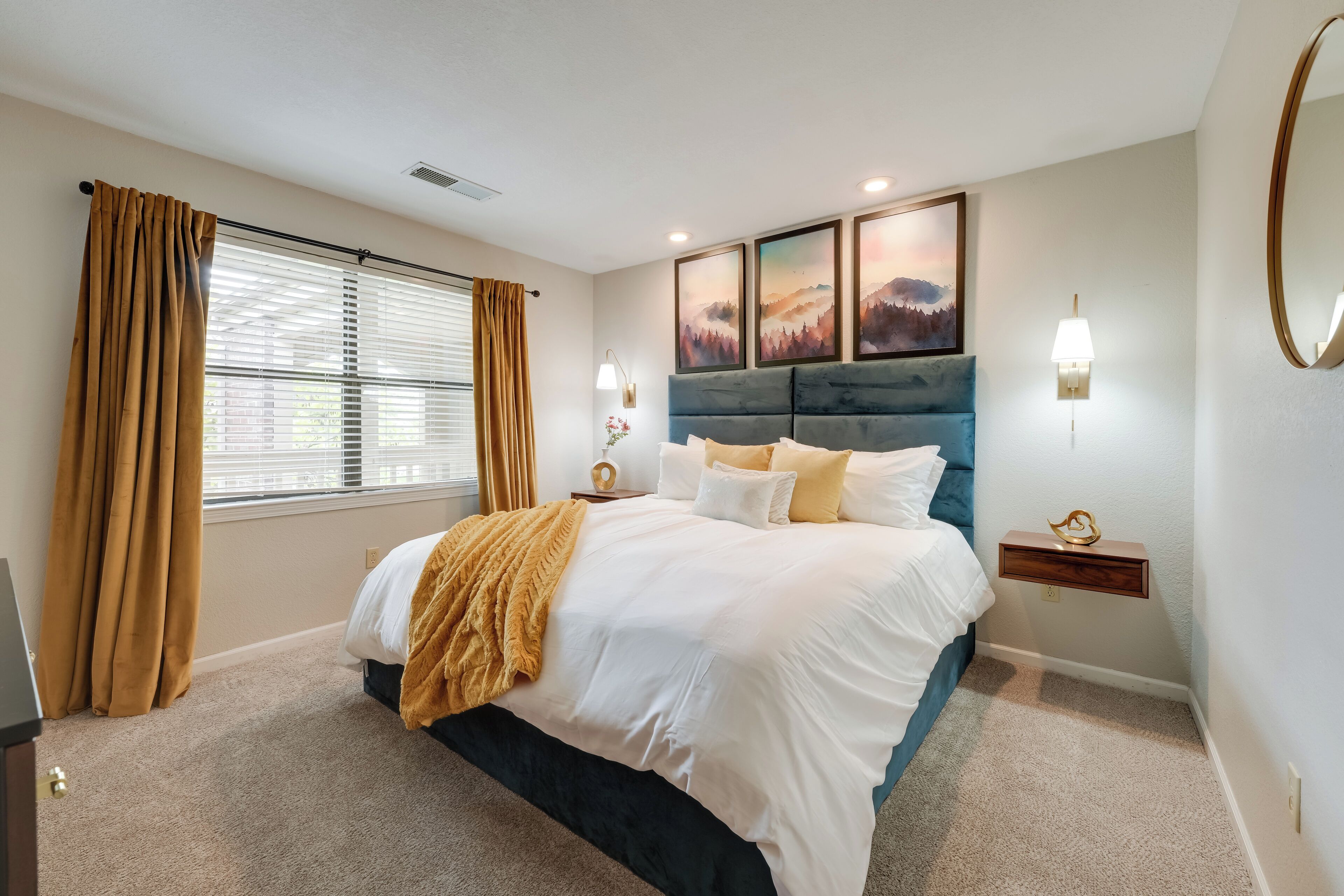 A bedroom with a bed, curtains, a nightstand, wall art, and a mirror.