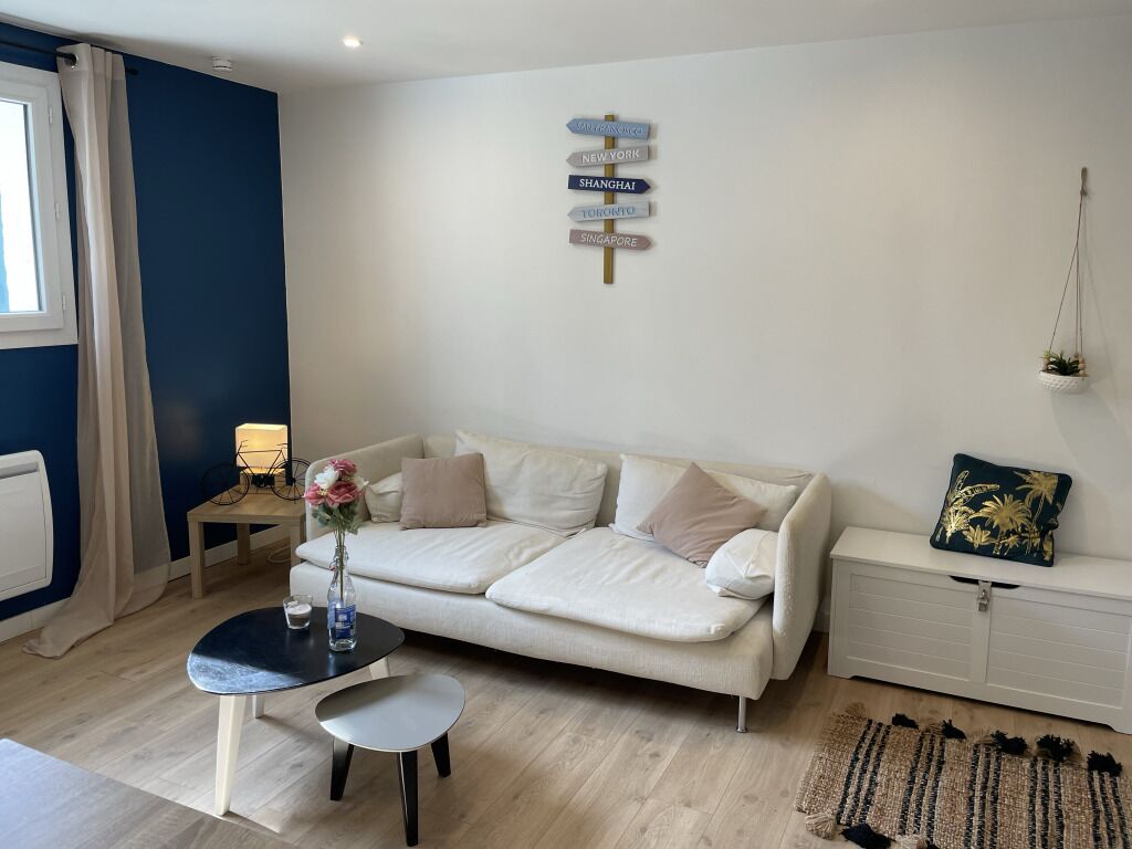 A modern living room with a white sofa, a small round table, a vase with flowers, and a wall-mounted sign with city names.