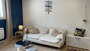A modern living room with a white sofa, a small round table, a vase with flowers, and a wall-mounted sign with city names.