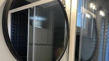A bathroom with a round mirror, a white sink, and a glass shower enclosure.