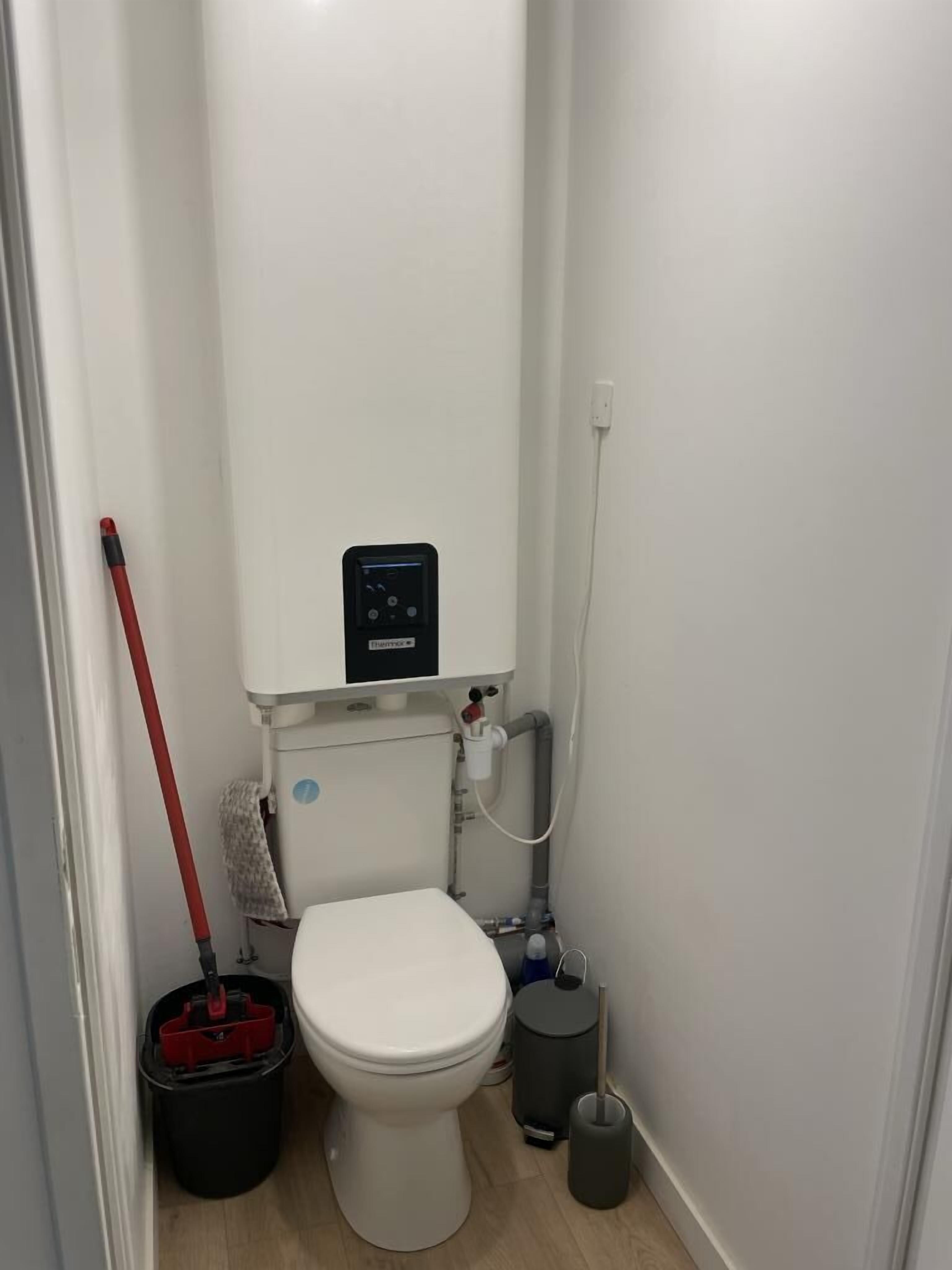 A small, compact bathroom with a white toilet, a black bidet, a red mop, and a trash bin.