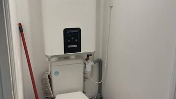 A small, compact bathroom with a white toilet, a black bidet, a red mop, and a trash bin.