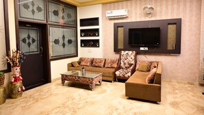 A living room with a sofa, armchair, and coffee table. There is a TV mounted on the wall and an air conditioning unit above it. - SPARSH CANOPY RESORT (Jaipur)