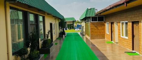 A corridor with green artificial grass, leading to multiple rooms with green roofs and beige walls.