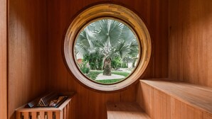 A wooden room with a circular window overlooking a garden with palm trees. - Pousada Pazuu (Ubatuba)