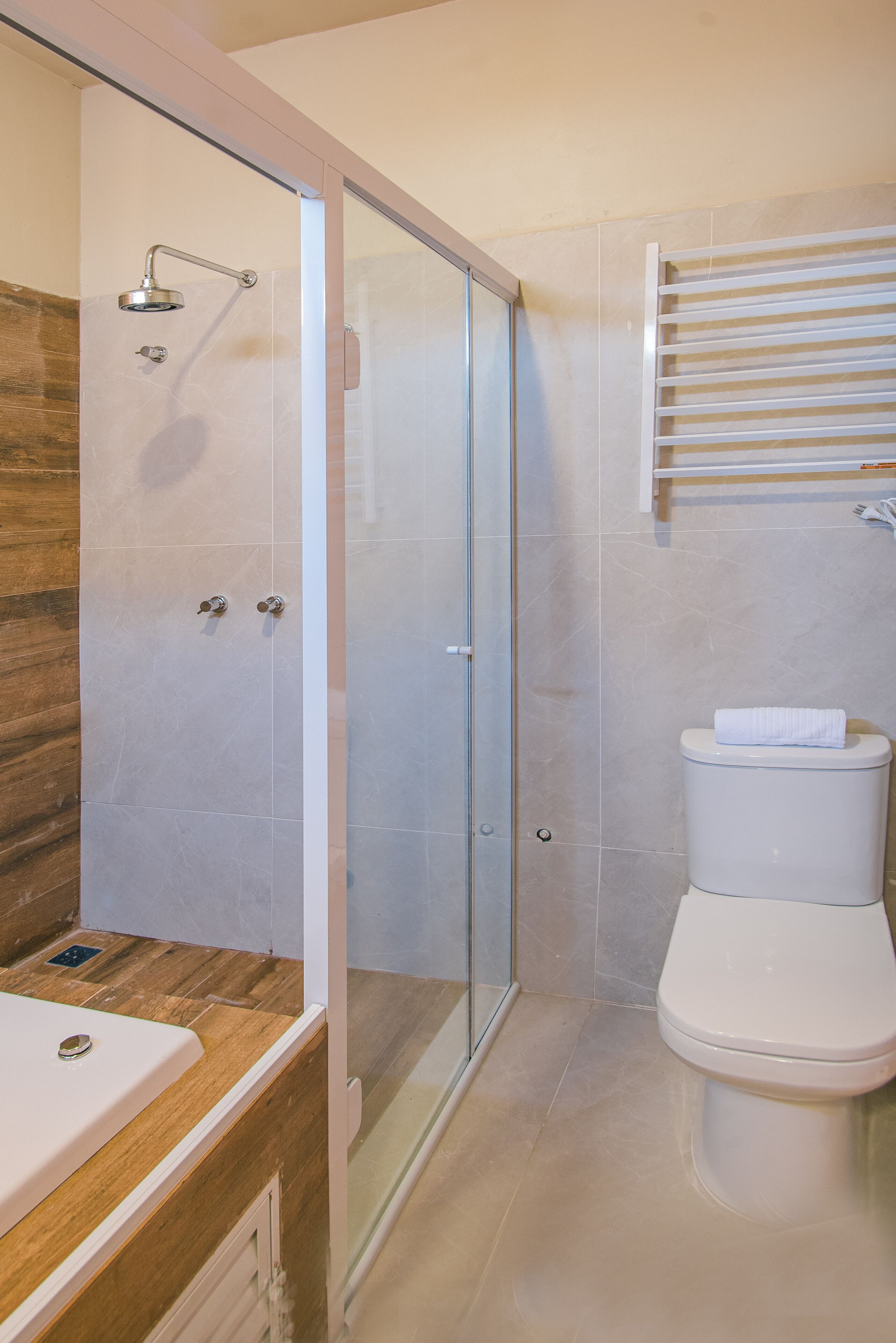 Un baño moderno con ducha envuelta en vidrio, tocador de madera y un inodoro blanco.