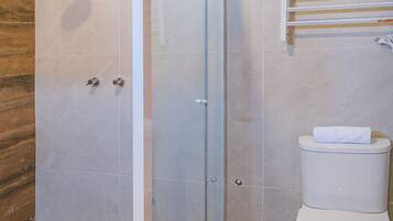 Un baño moderno con ducha envuelta en vidrio, tocador de madera y un inodoro blanco.