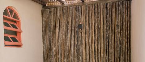A wooden bathtub in a room with a thatched roof, a wooden bench, and a small table with a laptop.