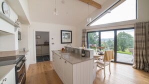 A modern kitchen with a large island, wooden flooring, and a view of the outdoors through large windows.