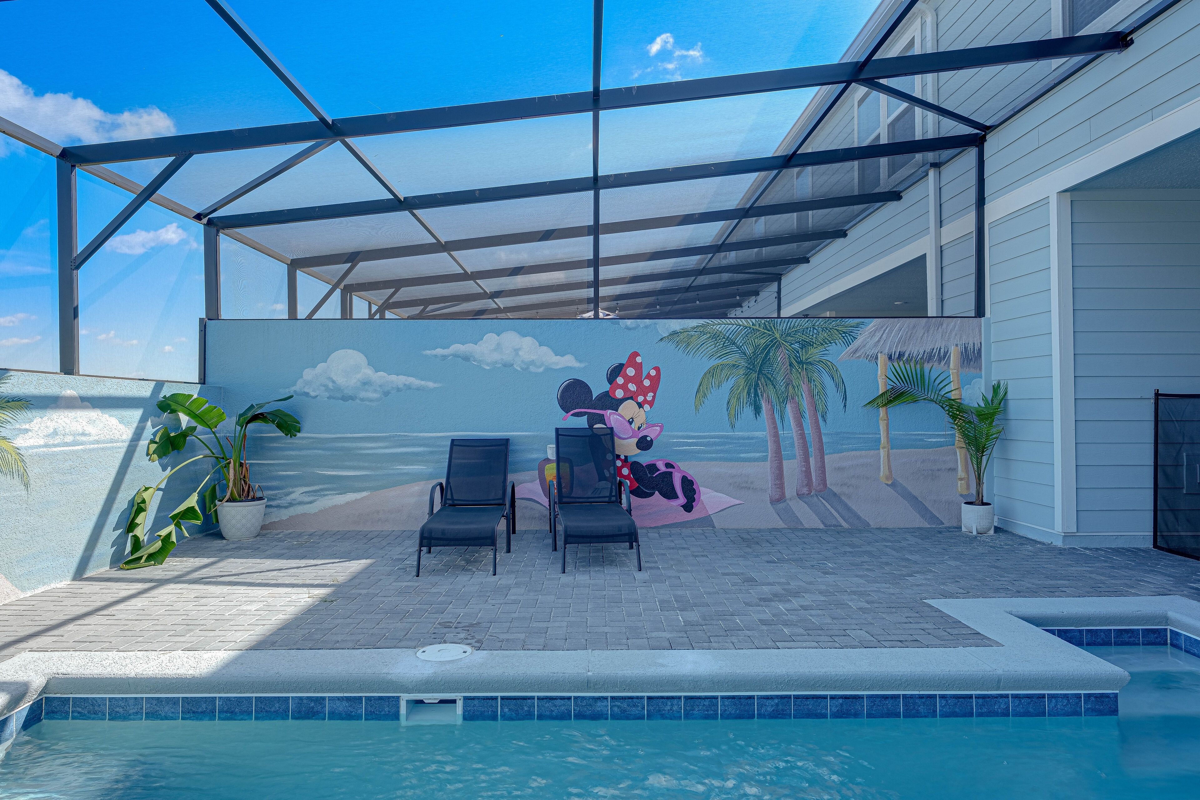 Un espace piscine intérieur doté de chaises longues, d’une fresque représentant une scène de plage et offrant une vue dégagée sur le ciel.