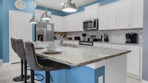 A modern kitchen with white cabinets, a granite countertop, stainless steel appliances, and bar stools. - 3725pcl-windsor Island Resort 5 Bedroom Townhouse by RedAwning (Davenport)