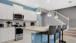 A modern kitchen with white cabinets, a granite countertop, stainless steel appliances, and a central island with bar stools. - 3725pcl-windsor Island Resort 5 Bedroom Townhouse by RedAwning (Davenport)