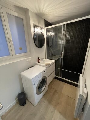 Ein kleines Badezimmer mit Waschmaschine, Waschbecken und Duschkabine.