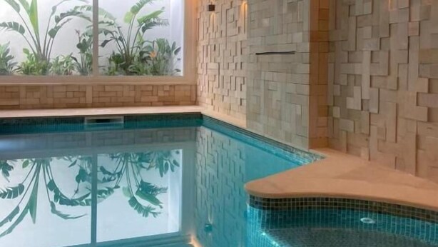 Ein moderner, überdachter Pool mit Blick auf üppige tropische Pflanzen vor den Fenstern.
